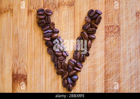 Lettera alfabetica V in chicchi di caffè tostati, resa 3D su sfondo tavola in legno Foto Stock