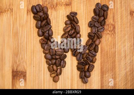 Lettera alfabetica W fatta con chicchi di caffè tostati, resa 3D su sfondo tavola in legno Foto Stock