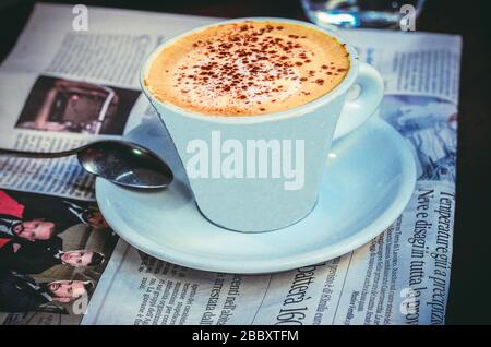 Una tazza di cappuccino appena fatto sul tavolo con giornale Foto Stock