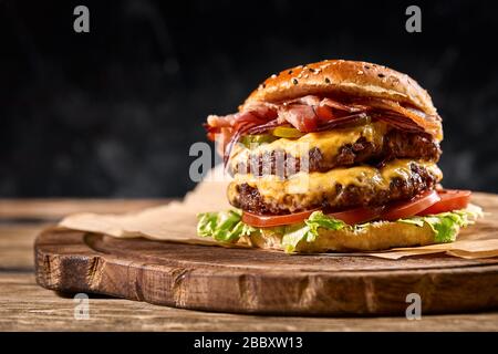 Succulento hamburger americano, hamburger o cheeseburger con due polpettine di manzo, con salsa e basato su sfondo nero. Concetto di fast food americano Foto Stock