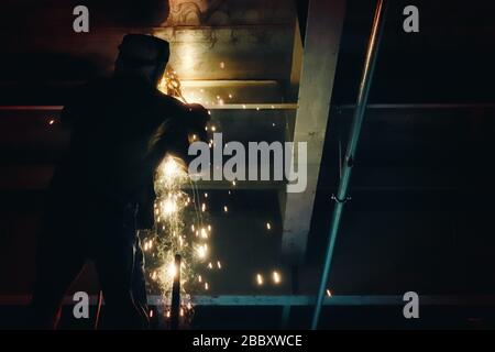 Saldatrice professionale in uniforme protettiva e maschera per saldatura di metalli nell'oggetto industriale. Foto Stock