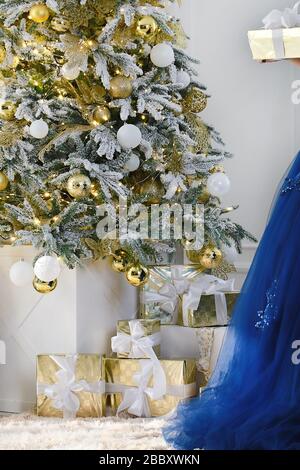 Regali di Natale sotto un albero di Natale decorato con sfondo bianco muro. Parte di elegante abito blu. Sfondo vacanza anno nuovo. Foto Stock