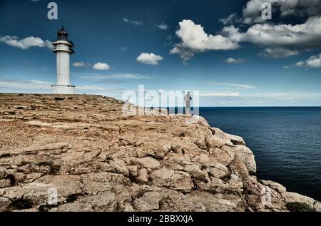 Faro sull'isola di Formentera, Spagna, il cielo blu con le nuvole bianche, la persona con una borsa sul bordo della roccia, pietre, tempo soleggiato Foto Stock