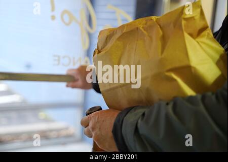 L'uomo spinge la maniglia della porta per uscire dal ristorante dopo aver ritirato un ordine di cibo (concentrarsi sul bordo del sacchetto di carta) Foto Stock