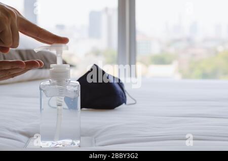 Pompando una bottiglia di gel alcolico per la pulizia della mano si mette a letto con maschera per la sanificazione a casa per proteggere il virus della corona infetto. Foto Stock