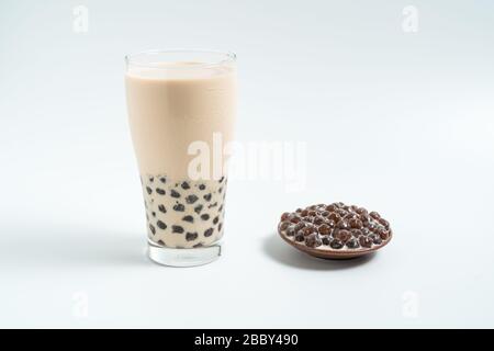 Un bicchiere di vetro di latte perla del tè (chiamato anche il tè di bolla) e una piastra di tapioca sfera su sfondo bianco. Perla del tè del latte è il più rappresentativo drin Foto Stock