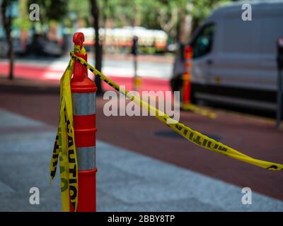 Nastro giallo di avvertenza legato al cono di sicurezza arancione sul marciapiede con furgone sullo sfondo Foto Stock