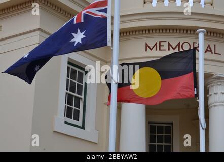 Bandiera aborigena che vola accanto alla bandiera nazionale australiana fuori da un monumento commemorativo nella città regionale Foto Stock