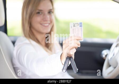 Giovane donna in auto mostra con orgoglio la patente di guida Foto Stock