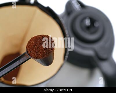 cucchiaio con polvere di caffè davanti alla succhieruola con caffè sullo sfondo. concetto di preparazione del caffè Foto Stock