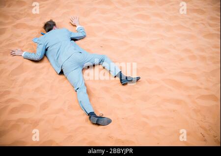 L'uomo d'affari inconscio sdraiato a faccia in giù crollato su sfondo deserto di sabbia rossa Foto Stock