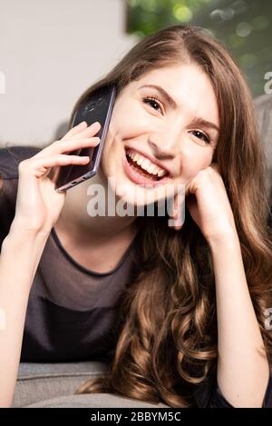 Giovane donna graziosa sta usando il suo smartphone sul telefono a casa Foto Stock