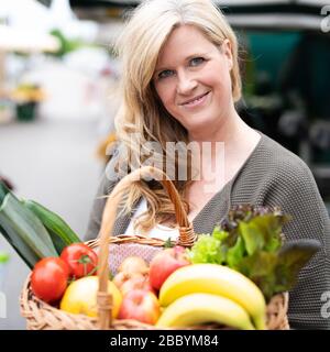 Una donna di mezza età con un sorriso positivo è lo shopping in un mercato settimanale Foto Stock