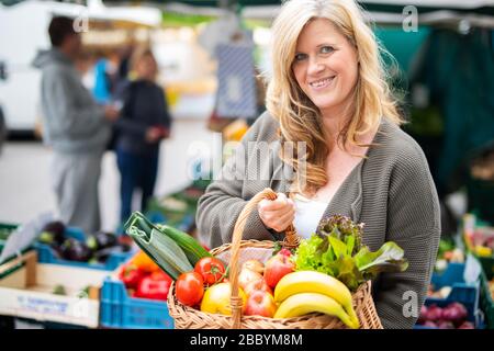 Una donna di mezza età con un sorriso positivo è lo shopping in un mercato settimanale Foto Stock