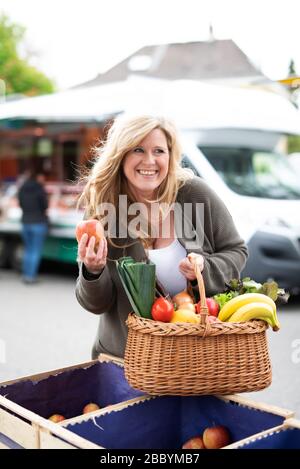 Una donna di mezza età con un sorriso positivo è lo shopping in un mercato settimanale Foto Stock