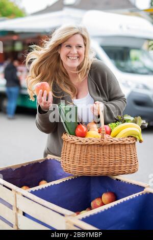 Una donna di mezza età con un sorriso positivo è lo shopping in un mercato settimanale Foto Stock