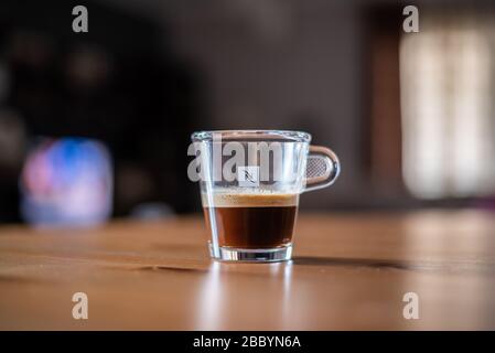 Bicchiere di caffè Nespresso trasparente su un tavolo con sfondo sfocato Foto Stock