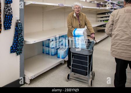 Signora anziana in supermercato con grande pacco di rotolo di servizi igienici nel suo carrello durante l'acquisto di panico di Coronavirus nel Regno Unito marzo 2020 Foto Stock