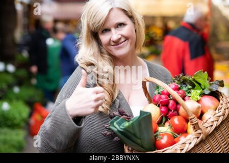 Una donna di mezza età con un sorriso positivo è lo shopping in un mercato settimanale Foto Stock