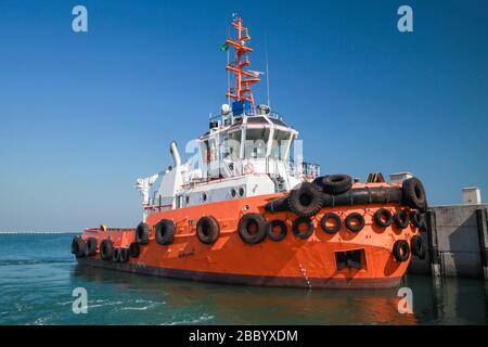Rimorchiatore con scafo arancione brillante è ormeggiato in un porto Foto Stock