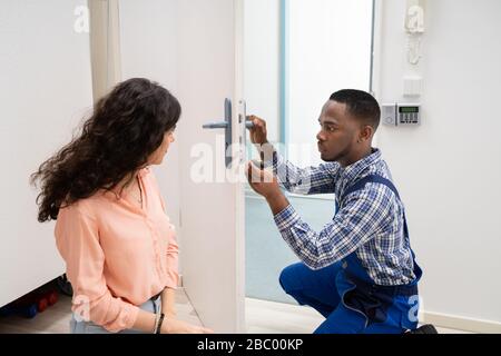 Donna sorridente guardando il tecnico che fissa la serratura della porta con un cacciavite a casa Foto Stock