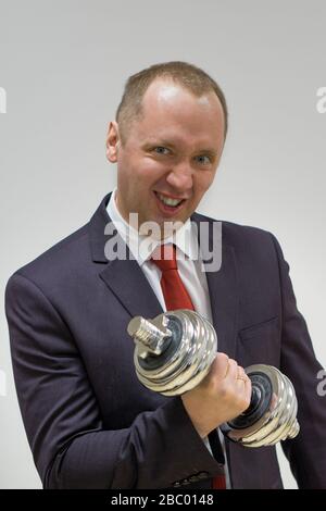 Ritratto di uomo d'affari sicuro sollevamento dumbbell su sfondo chiaro. Foto Stock