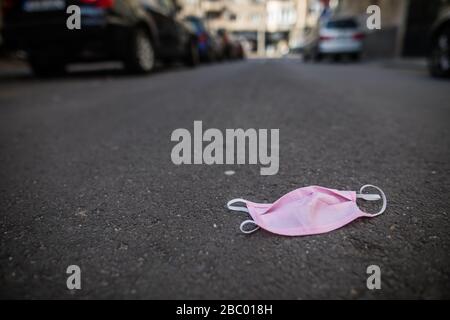 Una maschera di protezione del viso rosa usata è abbandonata sul pavimento. Foto Stock