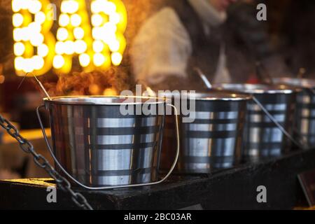 Street food. VIN brulé caldo. Vapore denso su secchi di vino caldo. Esterno. Foto ravvicinata. Foto Stock