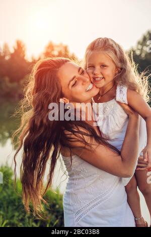 Giorno delle madri. Felice donna che gioca e divertirsi con piccola figlia nel parco primaverile tenendo capretto e ridendo. Famiglia Foto Stock