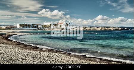 Il paesaggio del mare delle baleari e improbabile baia di bellezza, acqua azzurro, cielo con nuvole, edifici solitari è sullo sfondo, spiaggia senza persone Foto Stock