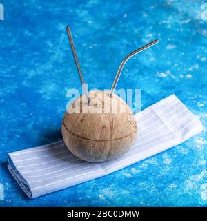 Cocco fresco con due paglia di metallo inserita in esso su tovagliolo da cucina a righe su sfondo blu. Zero rifiuti e nessun concetto di plastica. Rifiuto della plastica Foto Stock