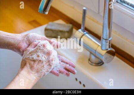 Vista ravvicinata sulle mani di una donna lavando accuratamente le mani con sapone sotto il rubinetto del lavello della cucina. Foto Stock