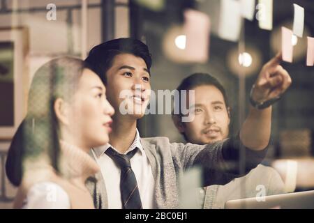 tre imprenditori asiatici di piccola impresa giovani imprenditori che meeing discutere in ufficio utilizzando le note adesive Foto Stock