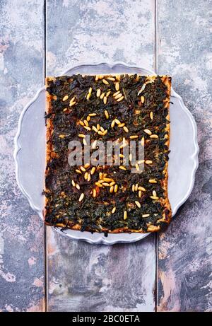 vista ad angolo di una fetta di coca de recapte, una tipica torta catalana simile alla pizza, fatta con spinaci, pinoli e uvetta, su un blu pallido Foto Stock