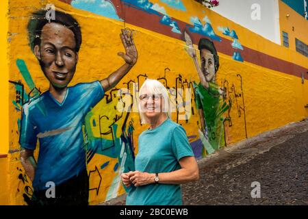 Sud Africa, Città del Capo, Schotsche Knoof, Bo Kaap, Wale St, turista femminile senior posto di fronte ai graffiti che fiancheggiano la ripida corsia acciottolata Foto Stock