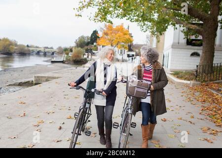 Sorridente donne anziane attive a piedi biciclette in autunno parco Foto Stock