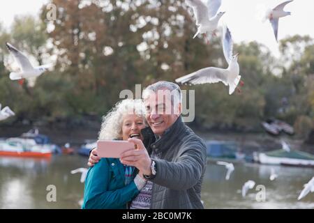 Giocosa coppia senior che prende selfie nello stagno nel parco Foto Stock