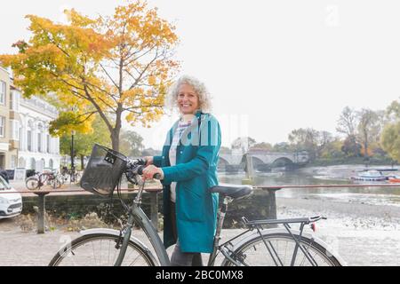 Ritratto sorridente donna anziana in bicicletta lungo il fiume autunno Foto Stock