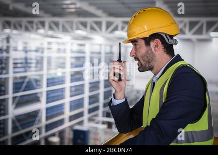 Supervisore maschile che parla, utilizzando walkie-talkie sulla piattaforma in fabbrica Foto Stock