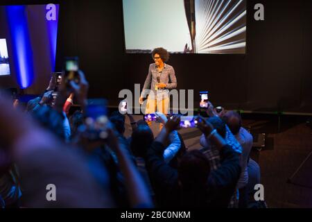 Pubblico con telefoni con fotocamera che fotografano l'altoparlante sul palco Foto Stock