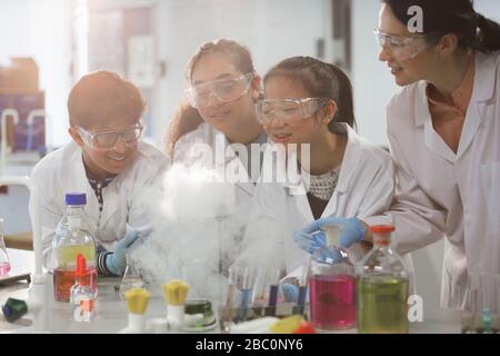 Insegnante femminile e studenti che guardano esperimenti scientifici reazione chimica in classe di laboratorio Foto Stock