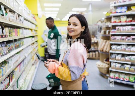 Ritratto sorridente, sicuro femmina drogheria con tablet digitale che lavora in supermercato Foto Stock