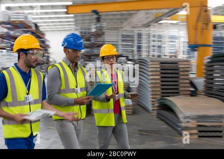 Supervisori e lavoratori con appunti e tablet digitali che camminano in fabbrica Foto Stock