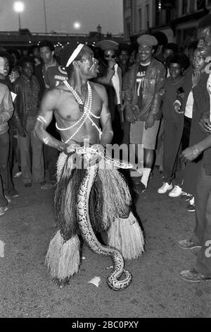 Notting Hill Carnival uomo vestito in 'nero costume africano con serpente dal vivo divertente una folla di appassionati di carnevale. 1980S UK 1981 HOMER SYKES Foto Stock