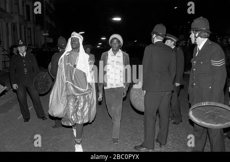 Notting Hill Carnevale 1980s. La polizia usa i coperchi dei bidoni della spazzatura come scudo per risolvere i problemi. Due rivelatori attraversano un gruppo di polizia. 1981 HOMER SYKES Foto Stock