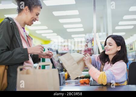 Cassa femminile che aiuta il cliente borse alimentari al supermercato checkout Foto Stock