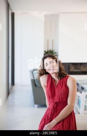 Ritratto donna bruna sorridente e sicura in abito rosso a casa Foto Stock