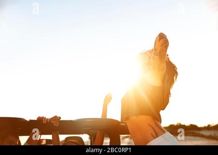 Giovane donna esuberante con tatuaggi sulla spiaggia soleggiata Foto Stock