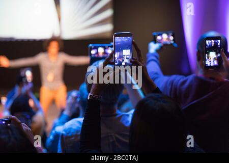 Pubblico con telefoni con fotocamera che fotografano l'altoparlante sul palco Foto Stock