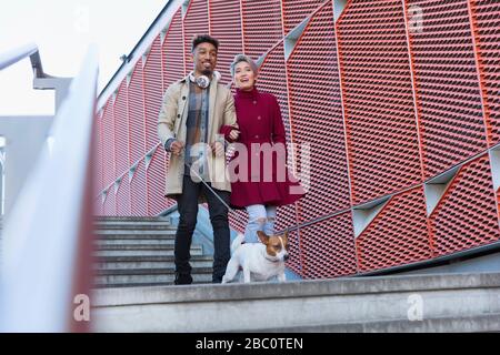 Giovane coppia sorridente che cammina cane giù urbano, scale moderne Foto Stock